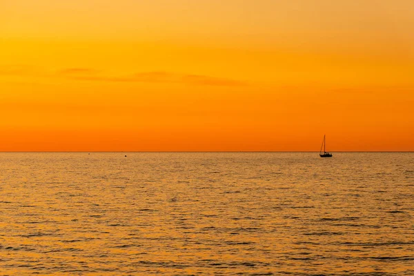 Yelkenliyle denizde turuncu ve sarı gün batımı. Alacakaranlıkta denizde yüzen bir teknenin minimalist fotoğrafı. Altın gün batımı ve yelkenli silueti sağda.
