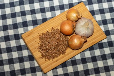 Sağlıklı besin maddelerine üst açılı bakış açısı: karabuğday, soğan ve siyah-beyaz kareli arka planda bambu hendeğinde sarımsak. Masada renkli soğan, karabuğday ve sarımsak