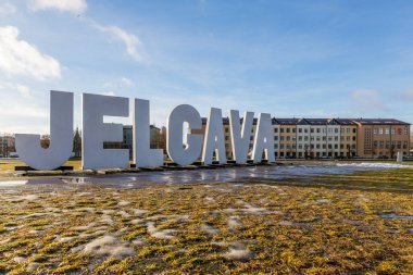 Low angle view to Jelgava city name sign in Post Island (Pasta sala), Jelgava, Latvia at sunny winter day. Jelgava city name sign, ice, frost, sun and blue sky clipart