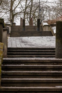Parktaki gri kış gününde beton sütunlar ve tuğla platformlarla yıpranmış kentsel beton merdivenlere dikey alçak açı. Tepeye çıkan eski kirli taş basamakların inşaatı. 
