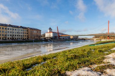 Letonya 'nın güneşli kış gününde donmuş Driksa nehri üzerindeki Mitava yaya köprüsüne alçak açılı görüş. Nehir kıyısından Jelgava 'ya kış manzarası. Baharda Post Island 'dan Jelgava, Letonya' ya görüntü.