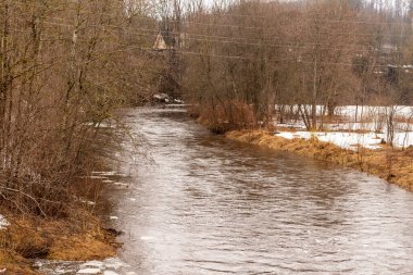 Yapraksız ağaçlar ve karlı çayırlarla çevrili küçük bir nehir. Bahar sabahının erken saatlerinde yağmurlu gride akan su akıntısı. Kışın akarsu yolu tepenin oradaki eve çıkar.. 