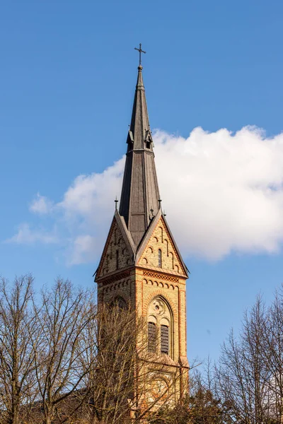 黑暗的黄色石头大教堂尖顶白云和蓝天背景 Torakalns教堂钟塔尖塔位于拉脱维亚里加 早春路德教会尖塔的垂直照片 — 图库照片