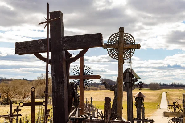 View from hill of crosses near iauliai, Lithuania to small pathway and surrounded meadow in cloudy spring day. Catholic crosses from back against sun. Old wooden crosses on the hill.