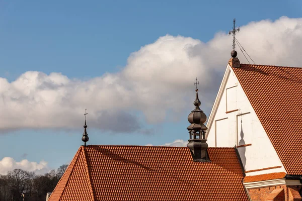 Three metal crosses at the red stone cathedral rooftops against light blue and white grey cloudy sky at early spring. Church roof with crosses. Catholic chapel rooftop with crosses at Kaunas, Lithuania.