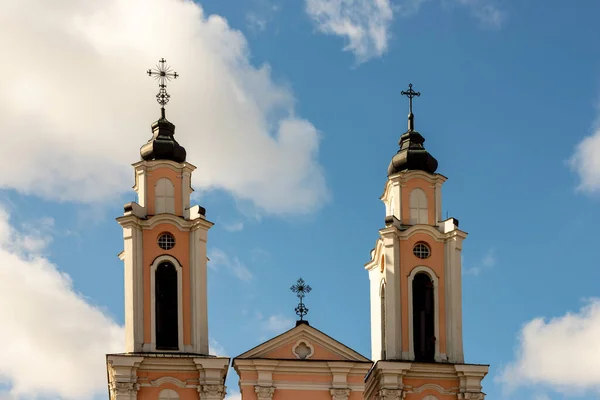 Kaunas, Litvanya 'daki Kutsal Haç Kuleleri Kilisesi. Barok beyaz ve turuncu renkli gökyüzü arka planında çan kuleleri. Roma Katolik Kilisesi çan kulesi.