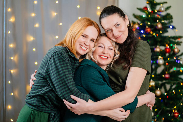three cheerful and happy friends hug at the Christmas tree. female friendship. 