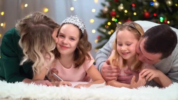 Una familia alegre y amigable escribe una carta a Santa Claus en el árbol de Navidad. — Vídeo de stock