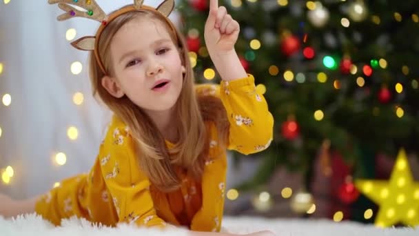 Ένα αστείο κοριτσάκι γράφει ένα γράμμα στον Άγιο Βασίλη στο χριστουγεννιάτικο δέντρο.. — Αρχείο Βίντεο
