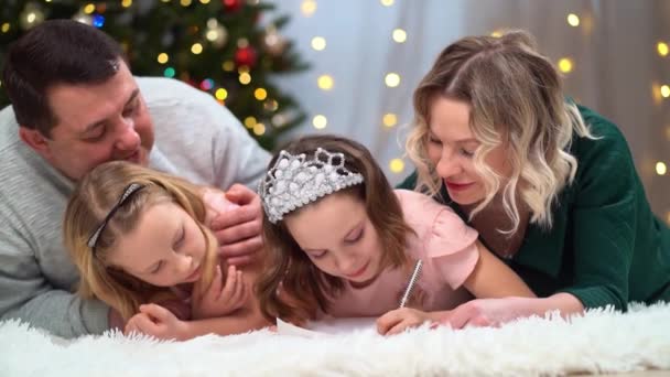 Eine fröhliche Familie schreibt einen Brief an den Weihnachtsmann am Weihnachtsbaum. — Stockvideo
