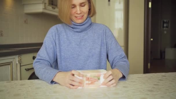 A woman in a blue sweater holds a large stack of rubles at home in the kitchen. — Stock Video