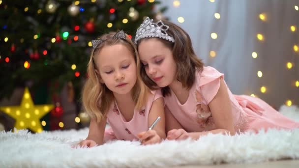 To vakre og lykkelige små jenter i rosa kjoler ved juletreet. – stockvideo
