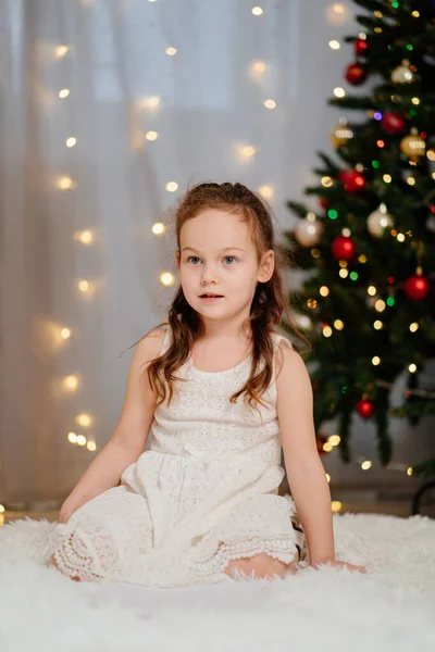 크리스마스 트리에서 하얀 드레스를 입은 아름답고 행복 한 작은 소녀. — 스톡 사진