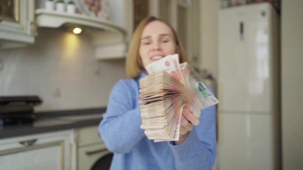 Uma mulher em uma camisola azul detém uma grande pilha de rublos em casa na cozinha. — Vídeo de Stock