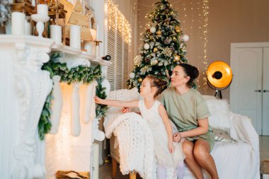 Anne ve kızı Noel ağacı ve şöminesinde çoraplarıyla birlikte kanepede oturuyor. 