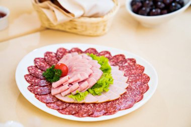 Doğranmış sosis, et, marul, otlar ve domatesli yuvarlak beyaz tabak.. 