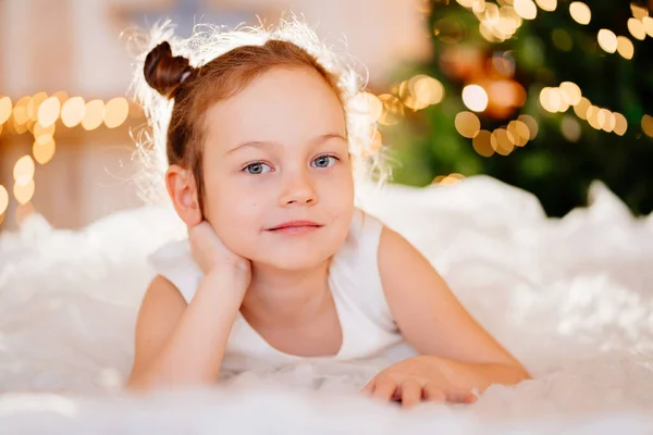 Uma menina engraçada em um vestido branco encontra-se em um tapete no quarto — Fotografia de Stock