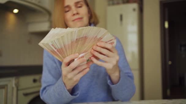 A woman makes a fan out of a large stack of rubles at home in the kitchen. — Stock Video