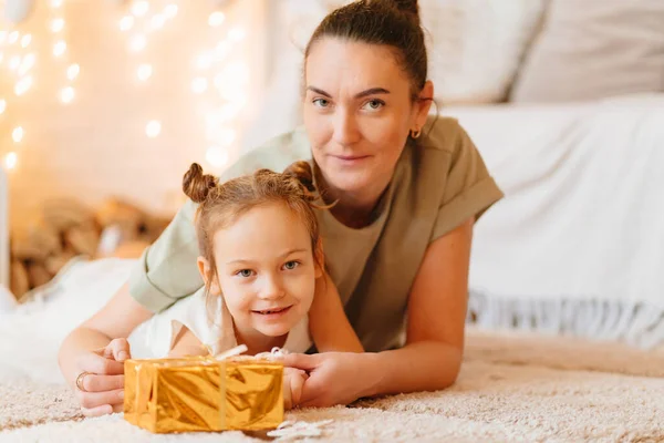 Mutter und lustige Tochter im weißen Kleid mit Geschenk in goldenem Geschenkpapier — Stockfoto