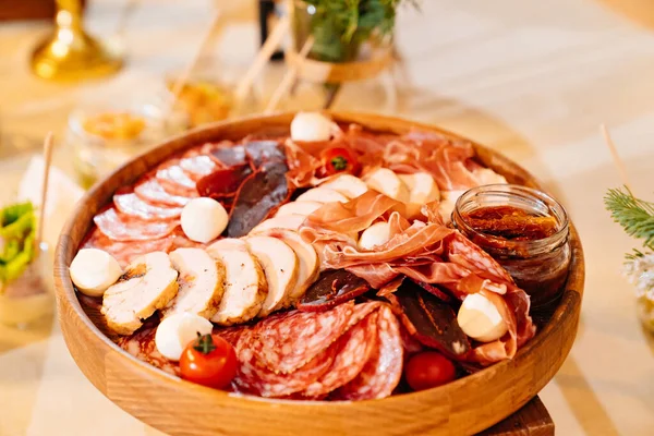 Różne mięso na okrągłym drewnianym talerzu z serem i pomidorami. — Zdjęcie stockowe
