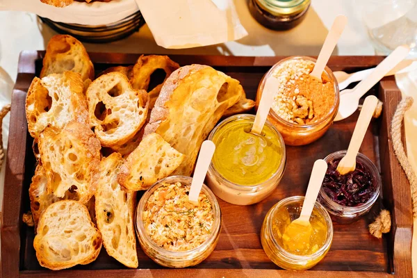 Wygodna porcja chleba z pasztetem w małych słoiczkach na drewnianej tacy. — Zdjęcie stockowe