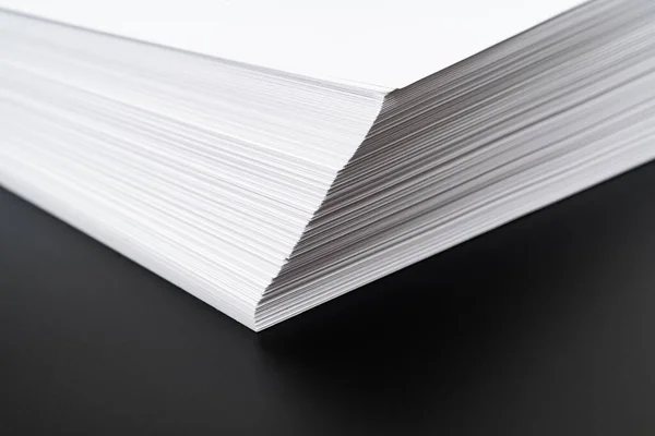 Крупным планом угол стека листов белой бумаги на черном фоне. Стоковая Картинка