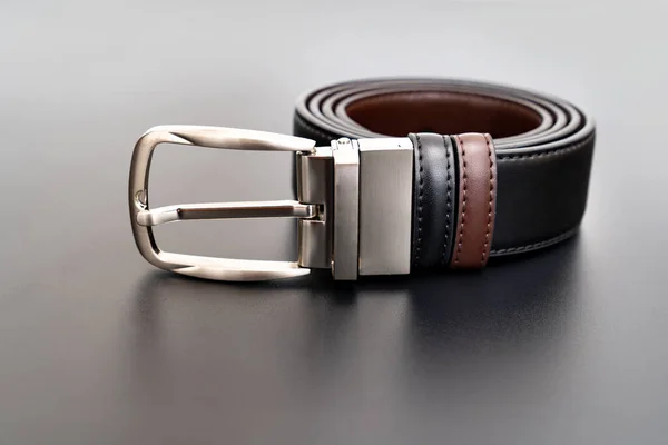 Double-sided black and brown leather belt with an unbuttoned buckle on a black. — Stock Photo, Image