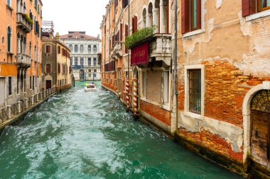 İtalya, Venedik 'teki evler arasında dar kanal boyunca seyreden bir motorlu tekne..