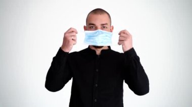 Genç yakışıklı sakallı adam maske takıyor ve kameraya bakıyor, ciddi bir şekilde.
