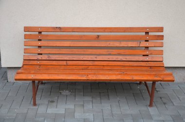 Evin yakınındaki duvara sırtı dönük, hafif bir yüzle rahat bir bank ayakta duruyor. Kahverengi boyalı, yatay tahta astarlı. Sırtlarına uyacak şekilde. Gri beton küplerin kaldırımı