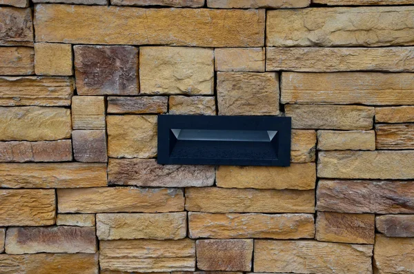 stone wall made of regular sandstone cladding. roughly hewn boards with a hidden lamp to the wall surface. it shines under the feet of pedestrians so that they do not trip over the night journey