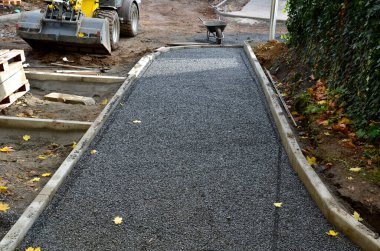 Asfalt inşaatı, temel beton kaldırımlar. İnşaat kazıcısı. İnşaatçılar yeni sokak yüzeyleri yapıyorlar. Fayanslar çakıl döşenecek. Sonbahar çalışma alanı. Kepçele, tekerlekler