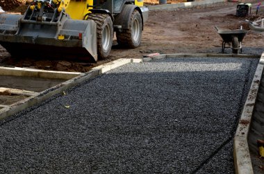 Asfalt inşaatı, temel beton kaldırımlar. İnşaat kazıcısı. İnşaatçılar yeni sokak yüzeyleri yapıyorlar. Fayanslar çakıl döşenecek. Sonbahar çalışma alanı. Kepçele, tekerlekler