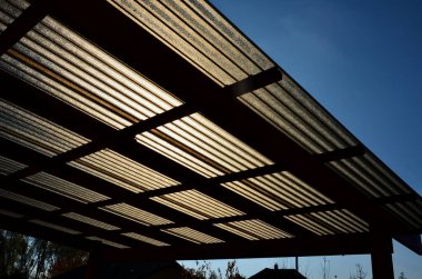 Evdeki teras güzel bir bahçede tel metal sandalyeler ve oval masadan yapılmış bahçe mobilyalarıyla donatılmıştır. Çatı kahverengi polikarbonat plastik dalgalı şekilli.