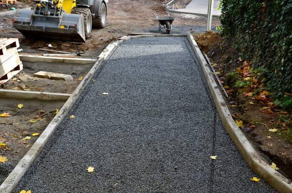 Строительство тротуаров, укладка бетонных бордюров в фундамент. строительный экскаватор. строители создают новые уличные поверхности. плитки будут уложены в гравий. Осеннее рабочее пространство. самокат, колеса