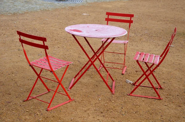 red chairs and round tables in a cafe on a cobbled square with a sand surface of compacted gravel. everything is made of light material that can be folded and cleaned every night. ice icing