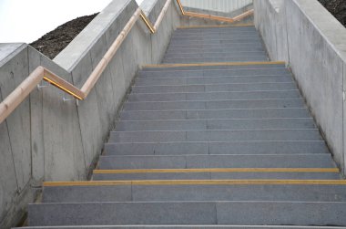 Sapının altından sarı ışıklı bir LED şerit çıkıyor. Gizli lamba bir adamın elini gösteriyor. Merdivenin beton tarafı, istinat duvarlarıyla yokuş aşağı gidiyor.