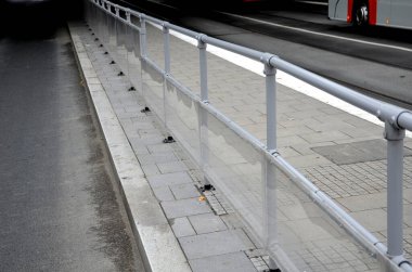 Otobüs platformu, gri metal bir boruya bağlı şeffaf pleksiglass tarafından korunuyor. İnsanlar geçen arabaların pisliğine bulanmaz.