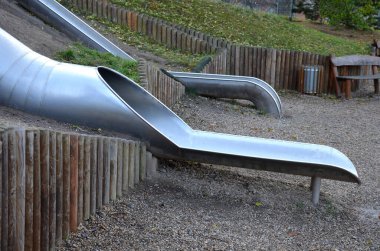 Çimenli tepeler ve ahşap çayırları olan paslanmaz çelik kaydırak. Tartan kauçuk pede çarpan kaygan çocuklar için büyük parlak bir tüp. Tüpün ucu açık bir yalaktır.