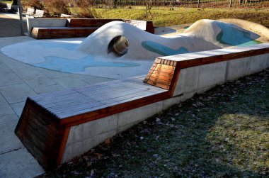 Tepeli, mavi-mavi-yeşil kauçuk manzara ve sahada renkli noktalar. Tepenin içinden paslanmaz çelik tünel. ahşap kaplanmış eğimli köşe bank istinat duvarı