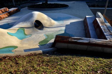 Tepeli, mavi-mavi-yeşil kauçuk manzara ve sahada renkli noktalar. Tepenin içinden paslanmaz çelik tünel. ahşap kaplanmış eğimli köşe bank istinat duvarı