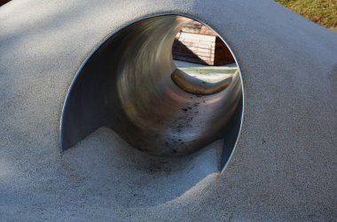 Tepeli, mavi-mavi-yeşil kauçuk manzara ve sahada renkli noktalar. Tepenin içinden paslanmaz çelik tünel. ahşap kaplanmış eğimli köşe bank istinat duvarı