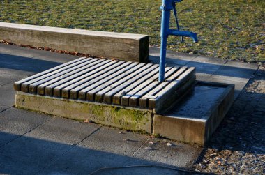 Mavi metal retro, parlak ahşap kapaklı. Su el pompasından taş yalağa akar. Bahçe tezgahı şekilli prizma çimenlik park mimarisi, dayanıklılık, ucuz