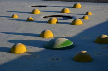Sarı kepçeli bir oyun alanının beyaz kauçuk yüzeyi ve insan ayak izlerinde renkli lekeler. Toplar, ahşap banklar ve dairesel trambolinler gibi yükseltilmiş lensler araziye gömüldü..