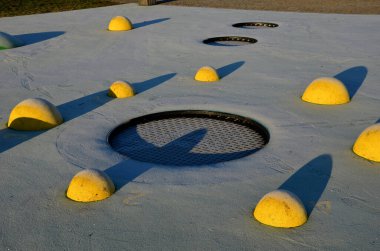 Sarı kepçeli bir oyun alanının beyaz kauçuk yüzeyi ve insan ayak izlerinde renkli lekeler. Toplar, ahşap banklar ve dairesel trambolinler gibi yükseltilmiş lensler araziye gömüldü..
