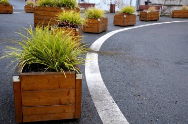 Meydanın yanındaki süs saksıları. Süslü çiçekli otlar. Tahta malzemeden yapılma saksı şeklindeki saksı. Masalı kamp tezgahı