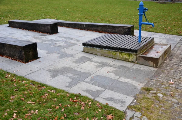 Mavi metal retro, parlak ahşap kapaklı. Su el pompasından taş yalağa akar. Bahçe tezgahı şekilli prizma çimenlik park mimarisi, dayanıklılık, ucuz