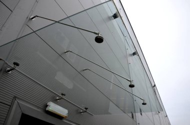 Endüstriyel binanın girişinin üstündeki cam çatı cephesinde metal kaplama var. Kalın duvarlı cam panel, metal çubuklarda, yuvarlak hedef tutucularla kapının üzerinde asılı.