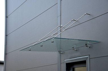 Endüstriyel binanın girişinin üstündeki cam çatı cephesinde metal kaplama var. Kalın duvarlı cam panel, metal çubuklarda, yuvarlak hedef tutucularla kapının üzerinde asılı.