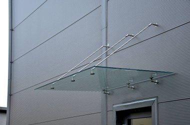 Glass roof above the entrance to the industrial building with metal cladding of the facade. thick-walled glass panel hangs above the door on metal rods with round targets holders clipart